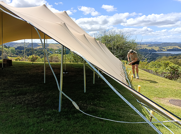 Mahurangi Harbour community marquee team member Kevin Finn preparing to take down the marquee the day after its first deployment for a wedding, on the Mahurangi West Hall marquee lawn